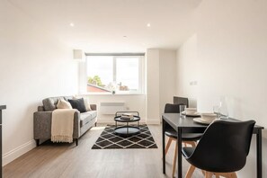 A modern living room with a sofa, a dining table with chairs, and a window with a view.