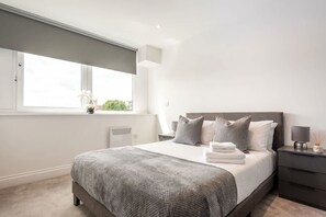 Un dormitorio moderno con una cama grande, una mesita de noche y un radiador. Se ve una ventana con vistas.