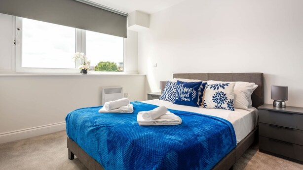 A modern bedroom with a large bed, a window with a view, and a bedside table with a lamp.