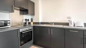 A modern kitchen with dark cabinetry, a built-in oven, a microwave, a coffee maker, and a toaster.