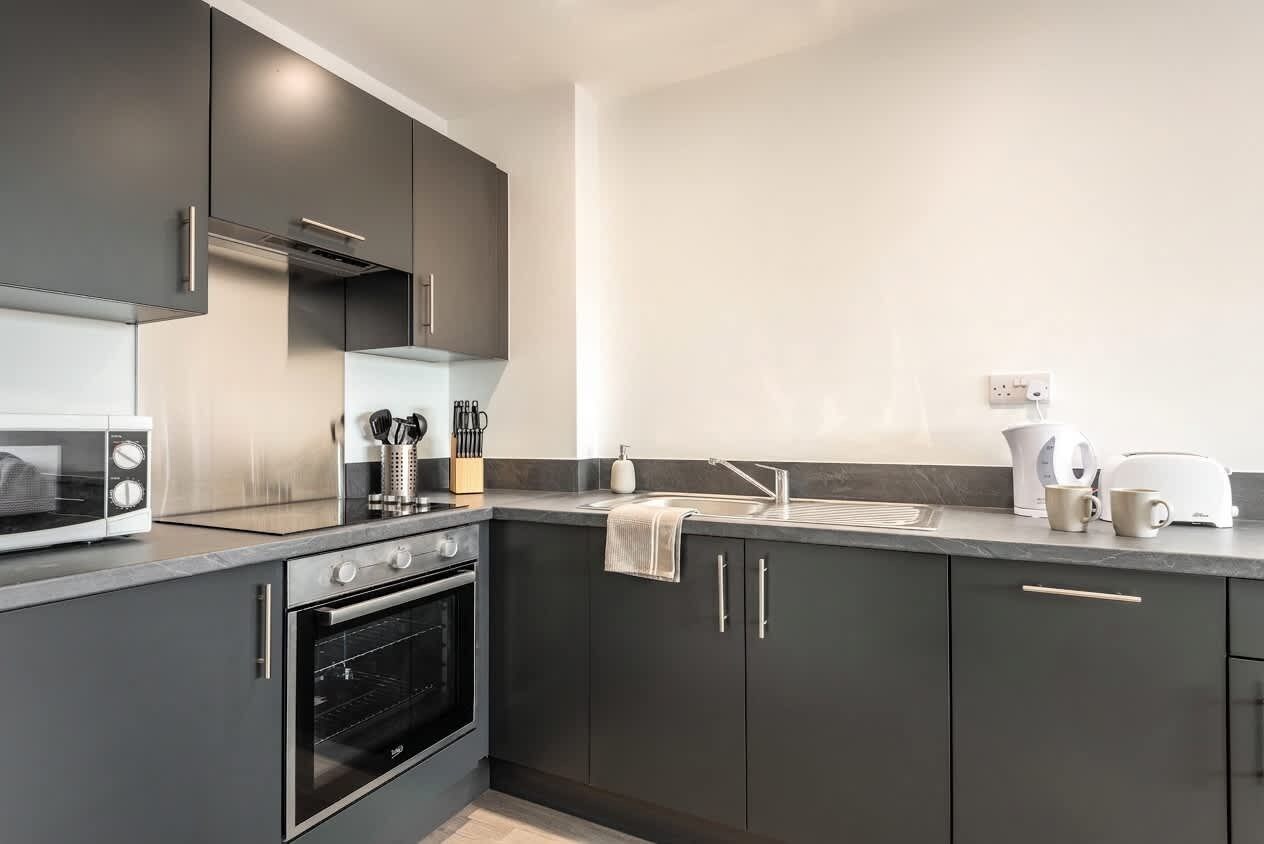 A modern kitchen with dark cabinetry, a built-in oven, a microwave, and a coffee maker.