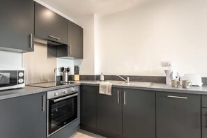 Una cocina moderna con armarios oscuros, horno empotrado, microondas y cafetera.
