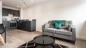 A modern kitchen with dark cabinets and a grey sofa with teal pillows.