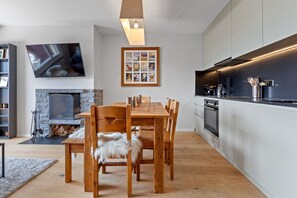 A modern kitchen with a built-in oven, a dining table with chairs, a stone fireplace, and a framed picture above the fireplace.