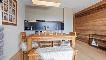 A modern kitchen with a wooden dining table, grey cabinets, and a wooden wall.