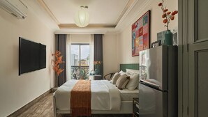 Une chambre d’hôtel équipée d’un lit, d’un téléviseur à écran plat, d’un réfrigérateur et d’une fenêtre avec des rideaux.