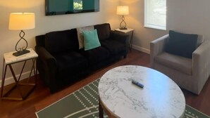 A living room with a black sofa, a grey armchair, a round coffee table, and two side tables with lamps. - 1BR WD Near BJ Hospital Forest Park Zoo (St. Louis)