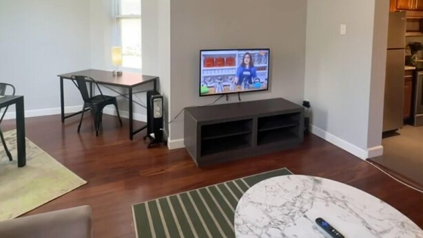 A living room with a TV on a stand, a dining table with chairs, a round coffee table, and a kitchen area visible through an open doorway. - 1BR WD Near BJ Hospital Forest Park Zoo (St. Louis)