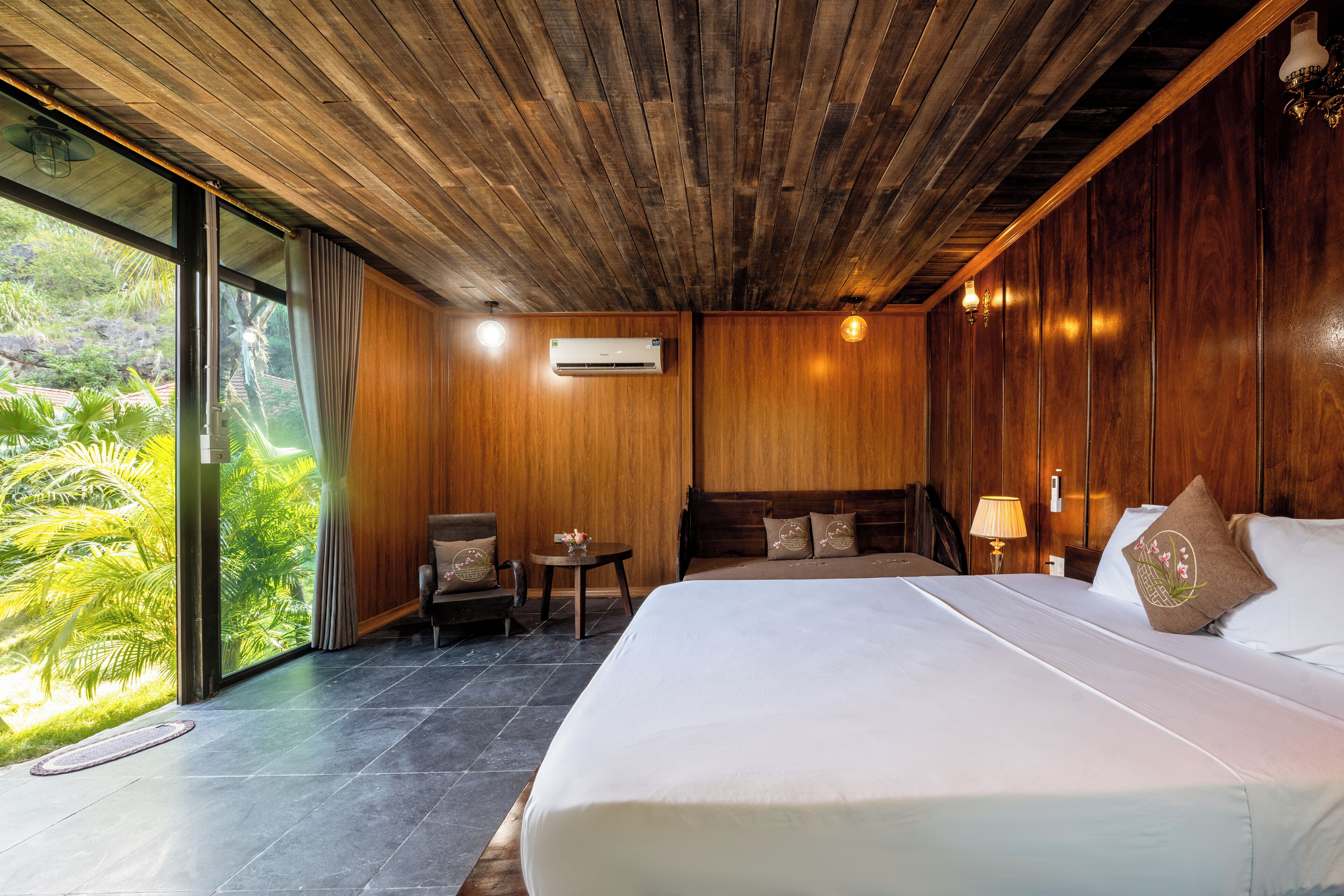 A hotel room with a large bed, wooden ceiling, and a view of greenery.