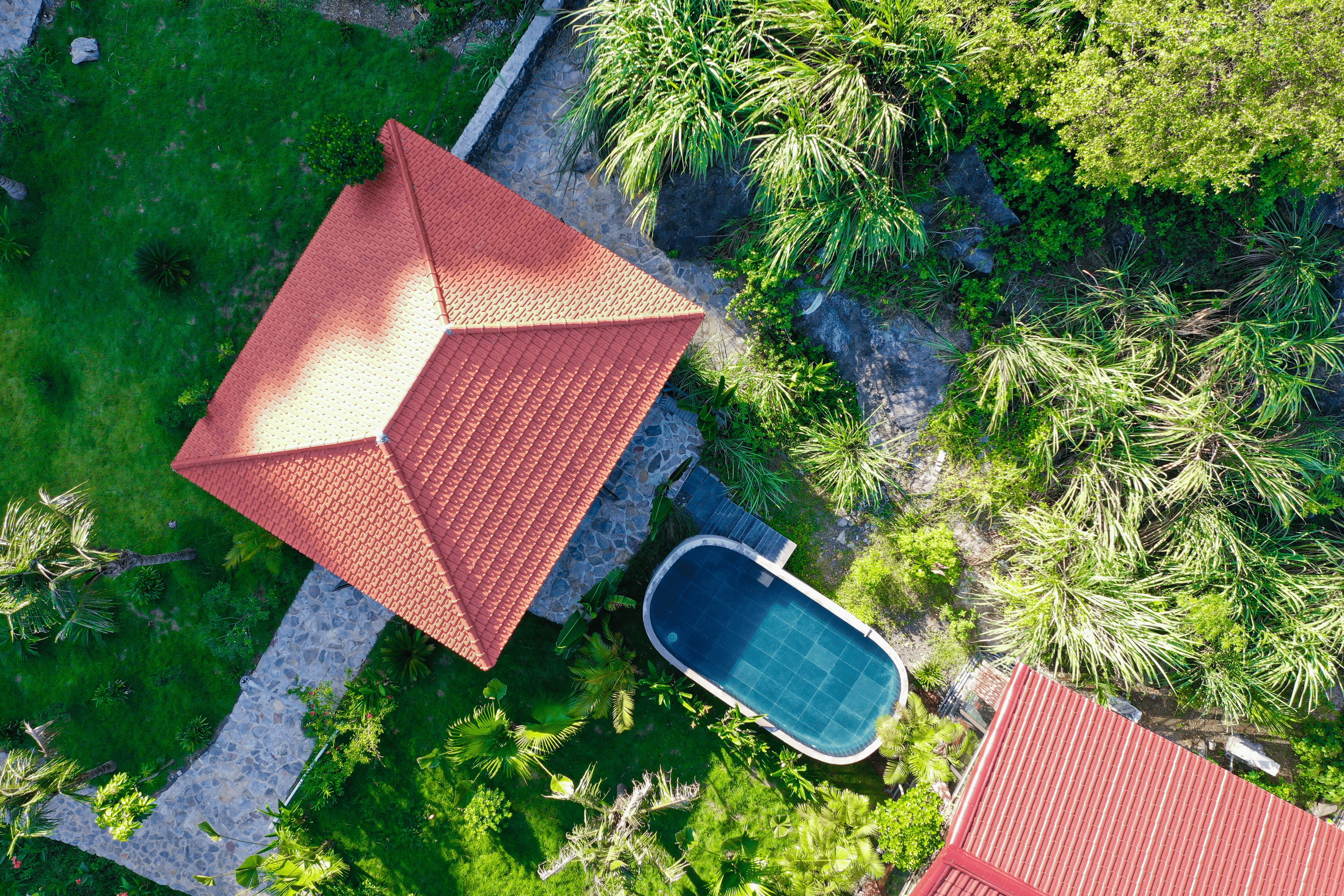 Vista aérea de una casa con techo rojo, piscina y vegetación exuberante.