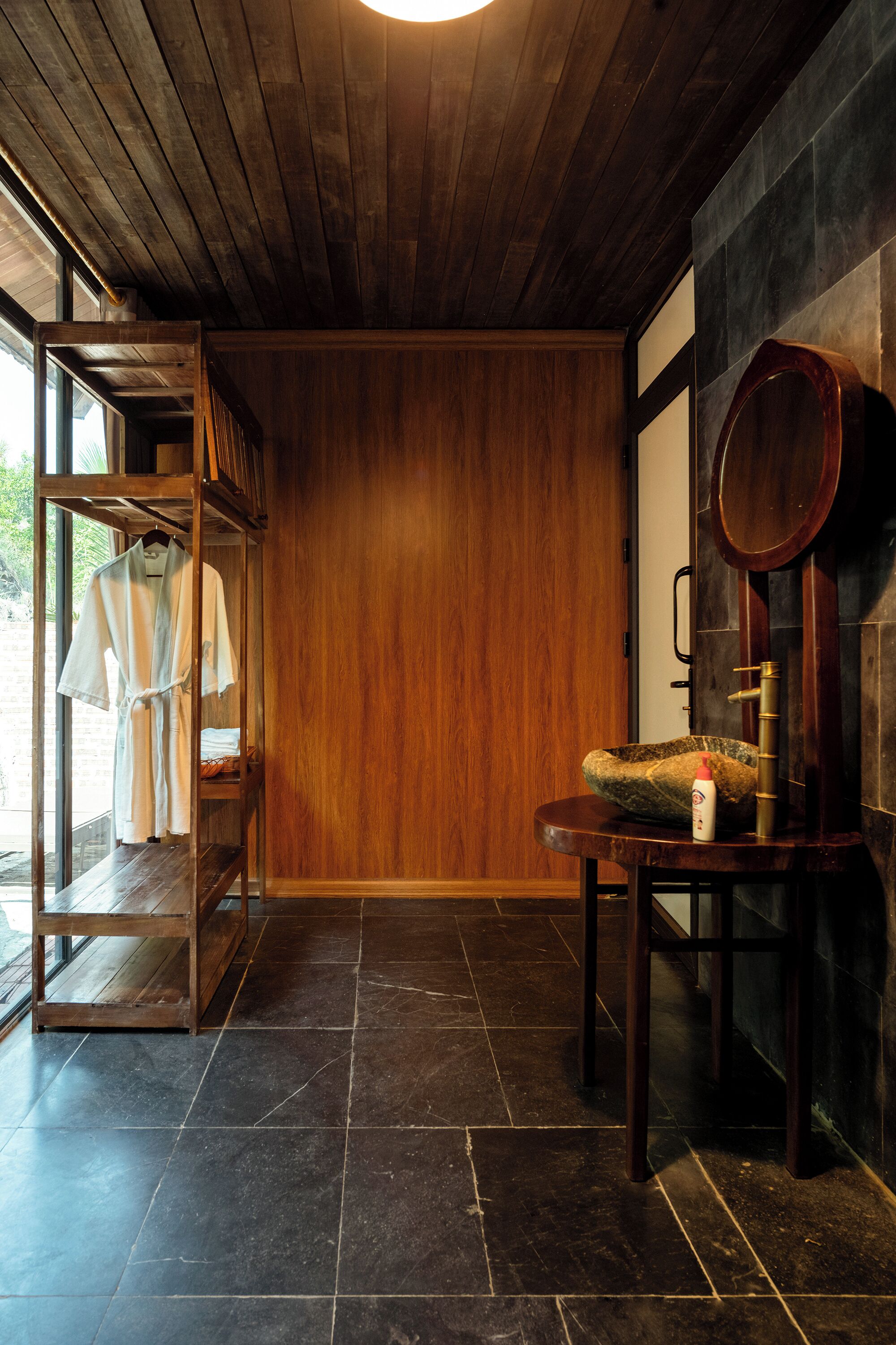 A wooden interior with a tiled floor, a wooden bench, a mirror, and a clothing rack with robes.