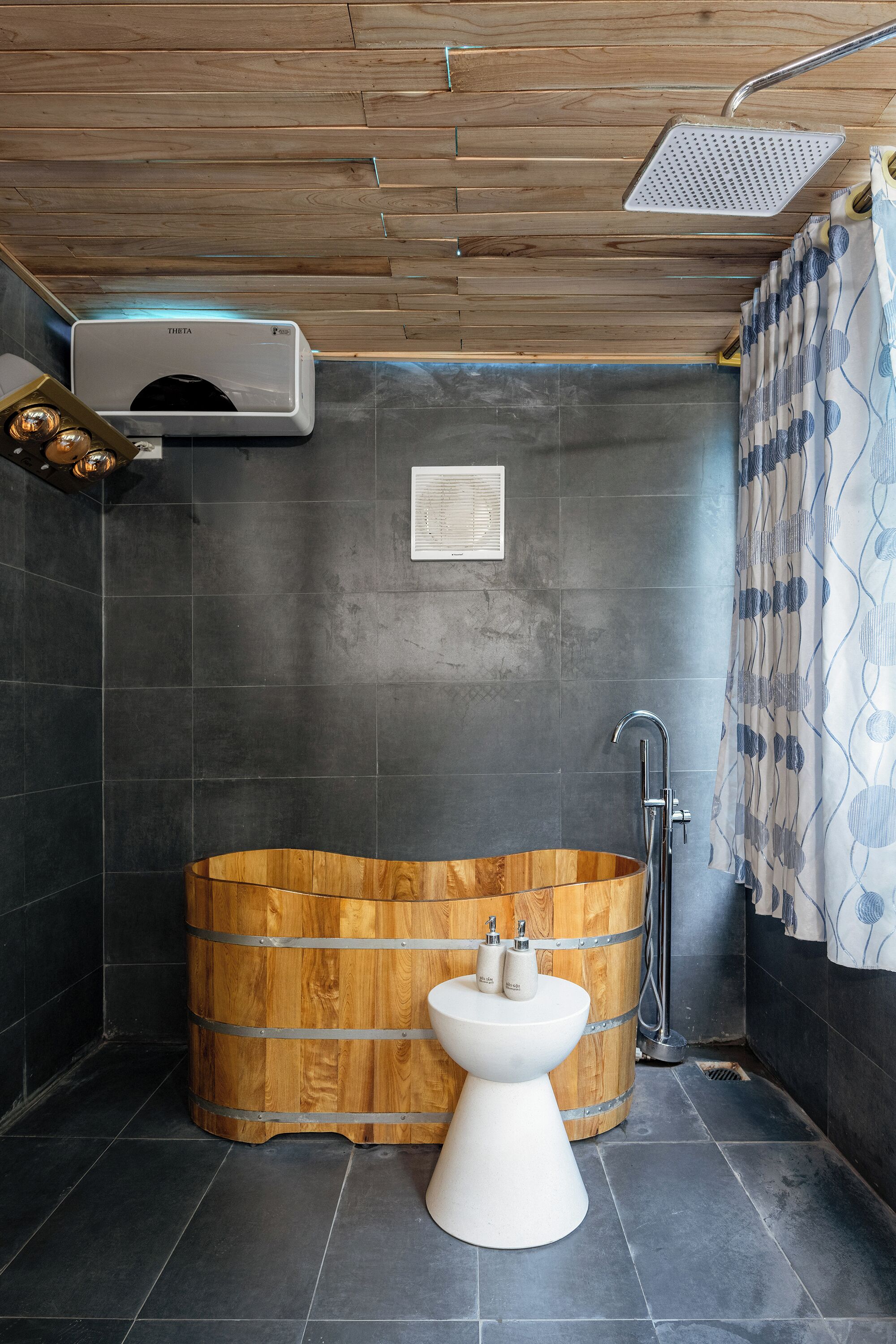 A modern bathroom with a wooden bathtub, a white pedestal sink, a handheld showerhead, and a towel rack.