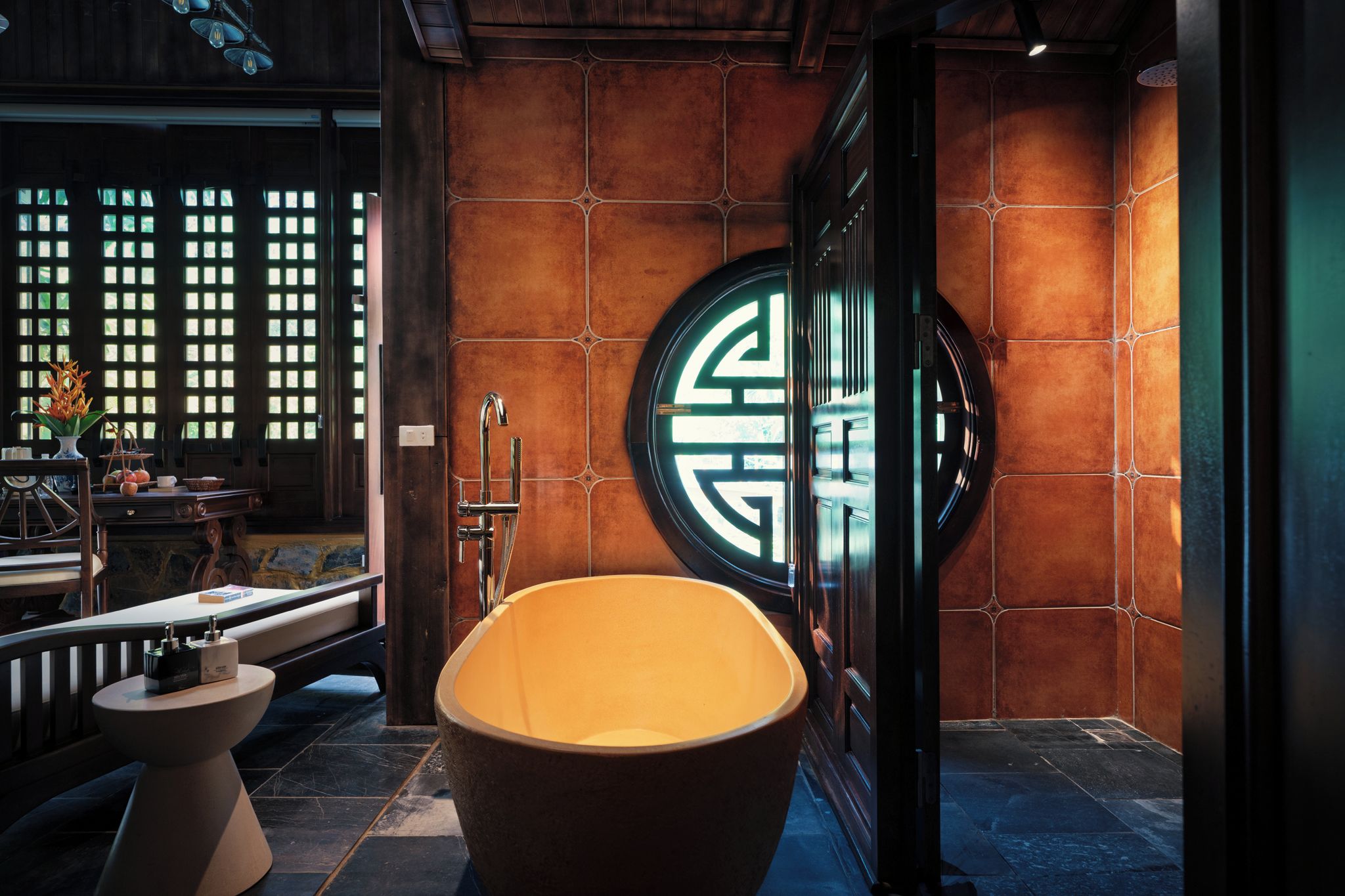 A modern bathroom with a freestanding bathtub, a round mirror with a geometric design, and a window with a grid pattern.