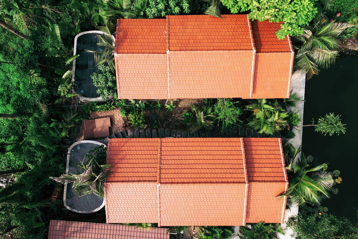 A large building with a tiled roof, surrounded by lush greenery and a body of water.