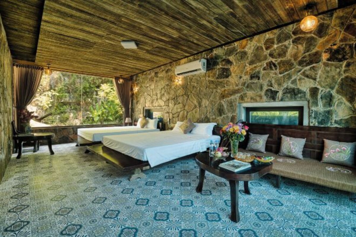 A room with two beds, a sofa, a coffee table, and a stone wall.
