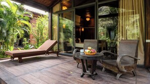 A wooden deck with a lounge chair, a table with fruit, and a rustic chair. - Trang An Garden Resort (Ninh Binh)