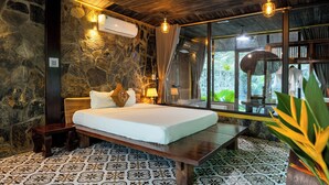 A bedroom with a stone wall, a wooden ceiling, a bed with white linens, a bedside table, and a window with curtains. - Trang An Garden Resort (Ninh Binh)