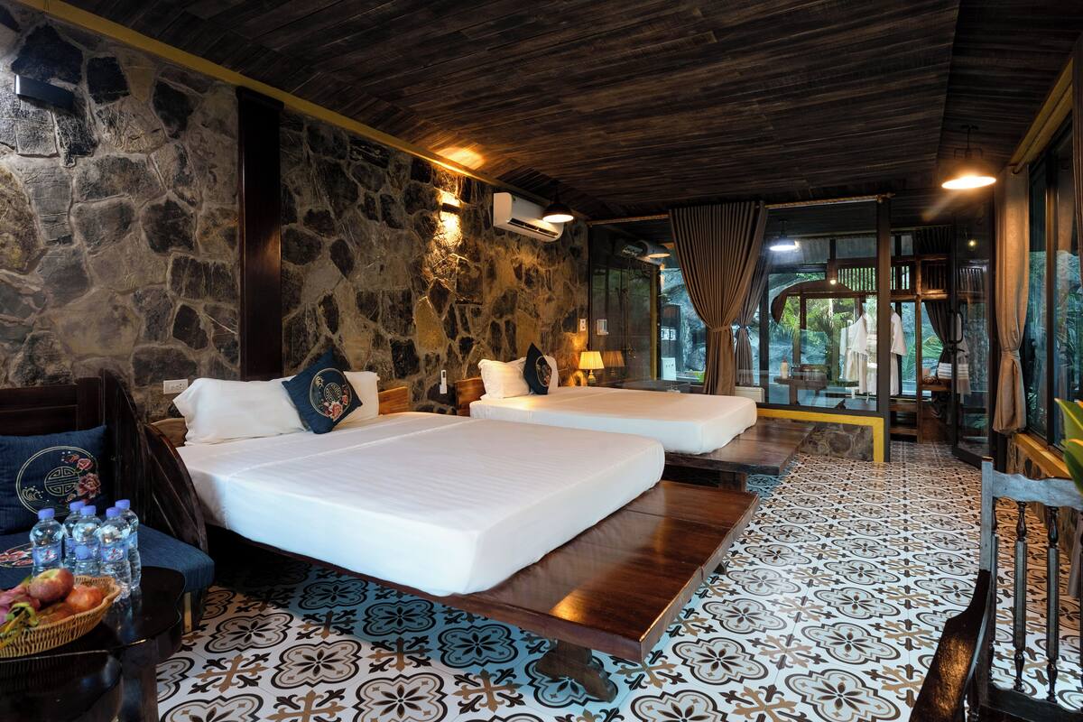 A room with two beds, stone walls, and a patterned floor.