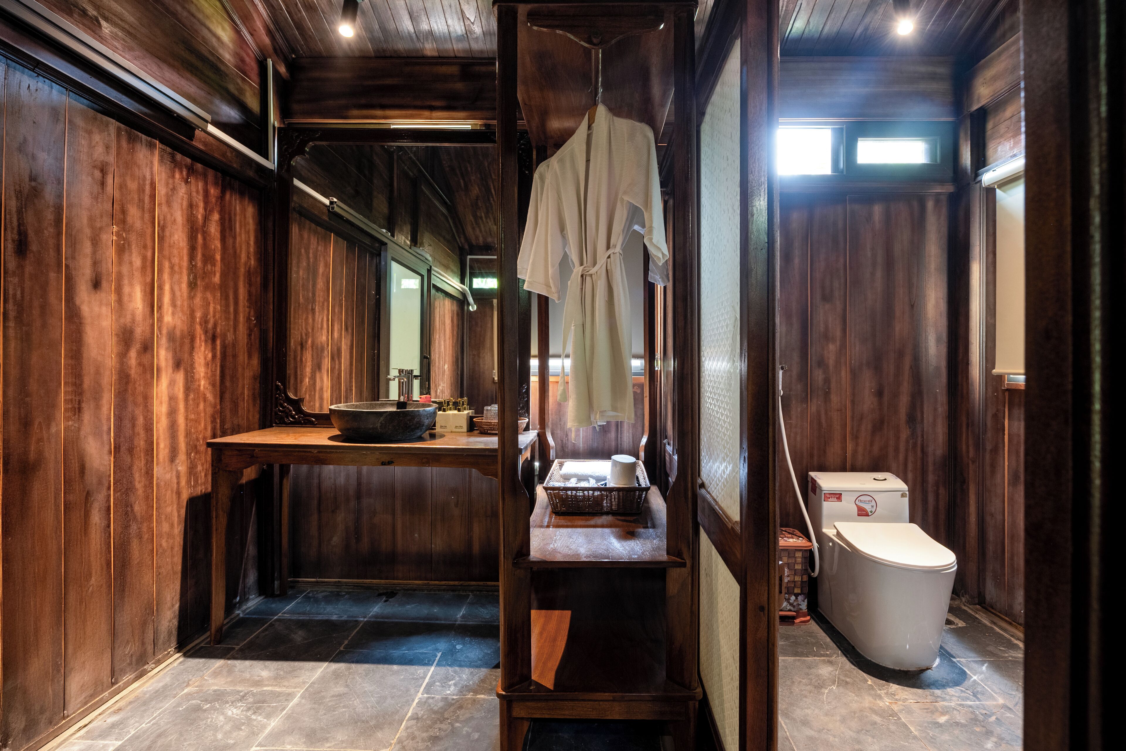A wooden interior with a sink, a white toilet, and a wooden table with a basket and a bowl.