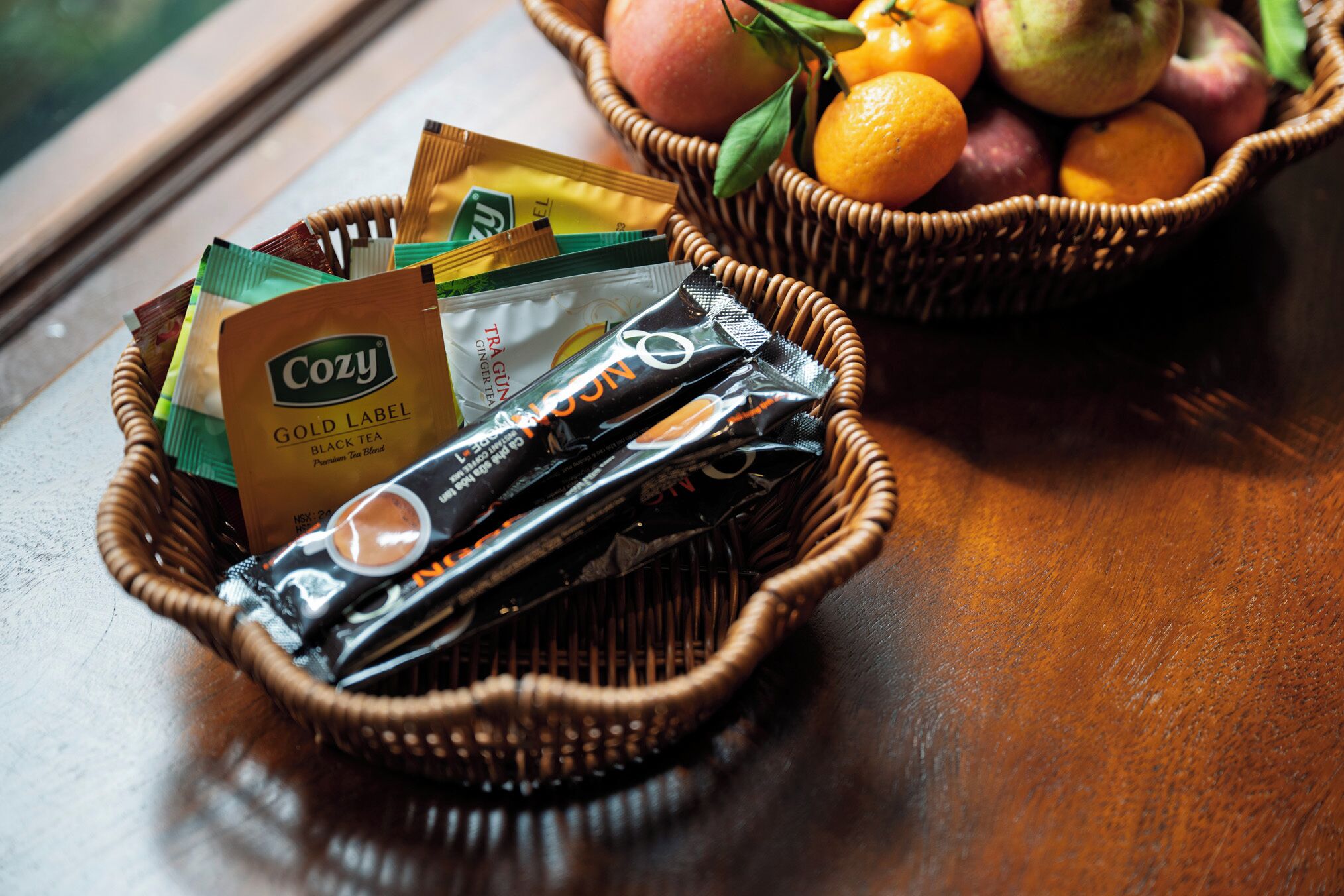 A wicker basket filled with tea bags and a basket of fruits.