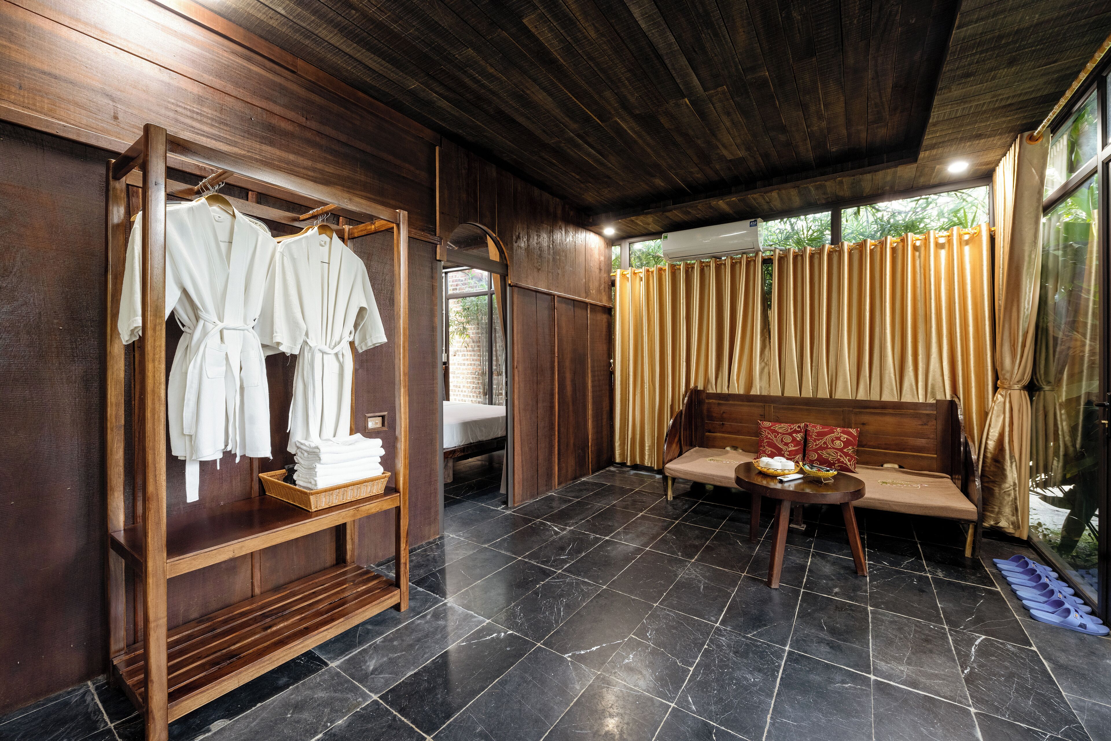 A room with a wooden wardrobe, a bed, a sofa, and a tiled floor.