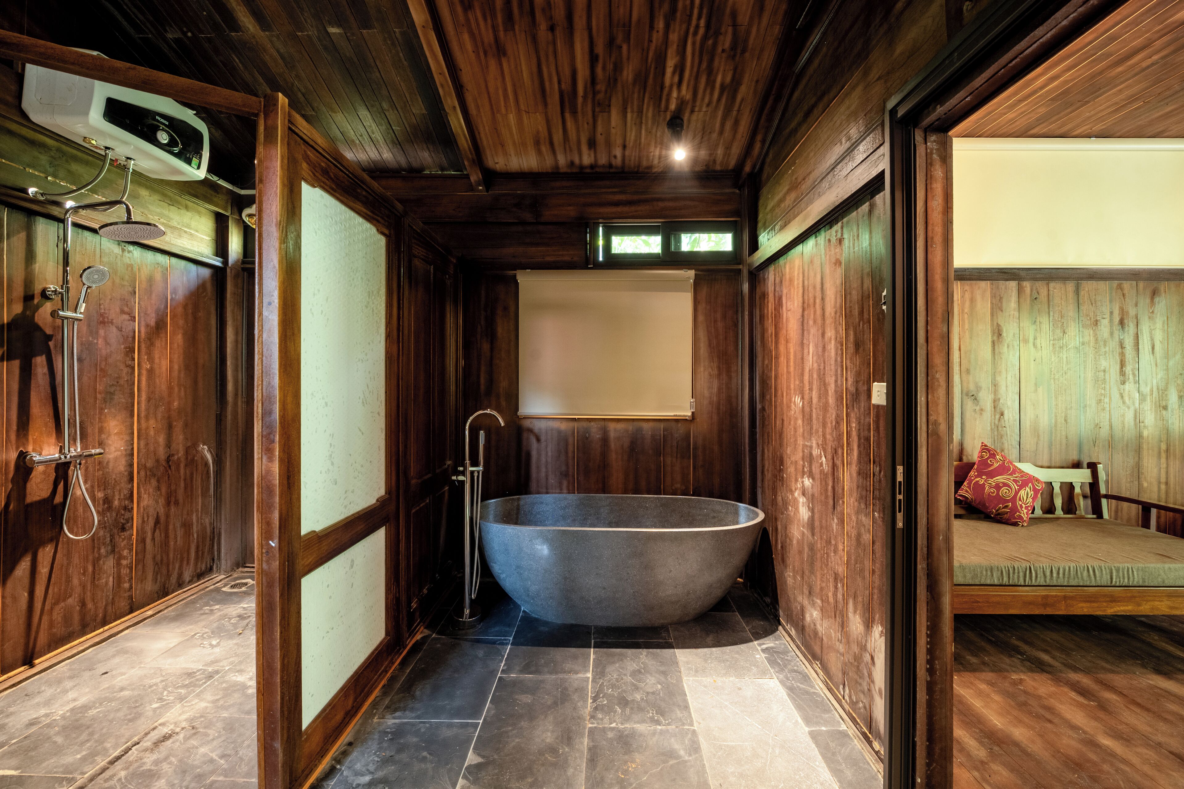 A wooden interior with a freestanding bathtub, a shower, and a bed with pillows.