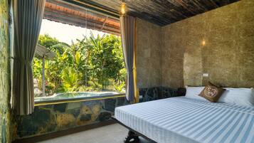 Un dormitorio con cama, cortinas, pared de piedra y vistas al verdor.