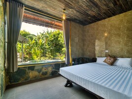 Un dormitorio con cama, cortinas, pared de piedra y vistas al verdor.
