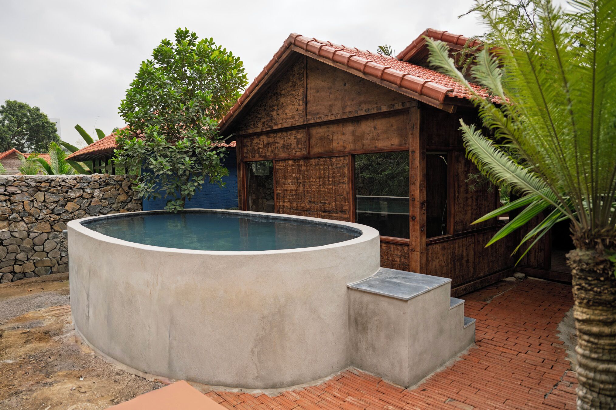 Une maison en bois avec une piscine, un mur en pierre et un palmier.