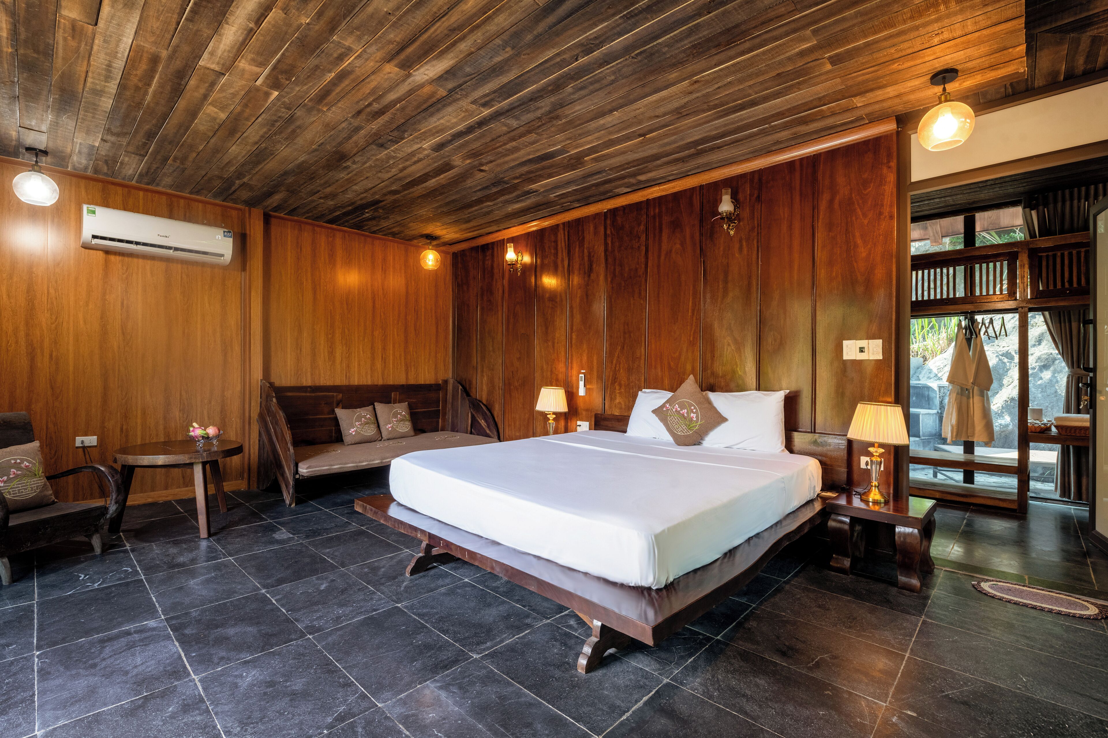 A bedroom with a large bed, wooden walls, a wooden ceiling, and a view of the outdoors.