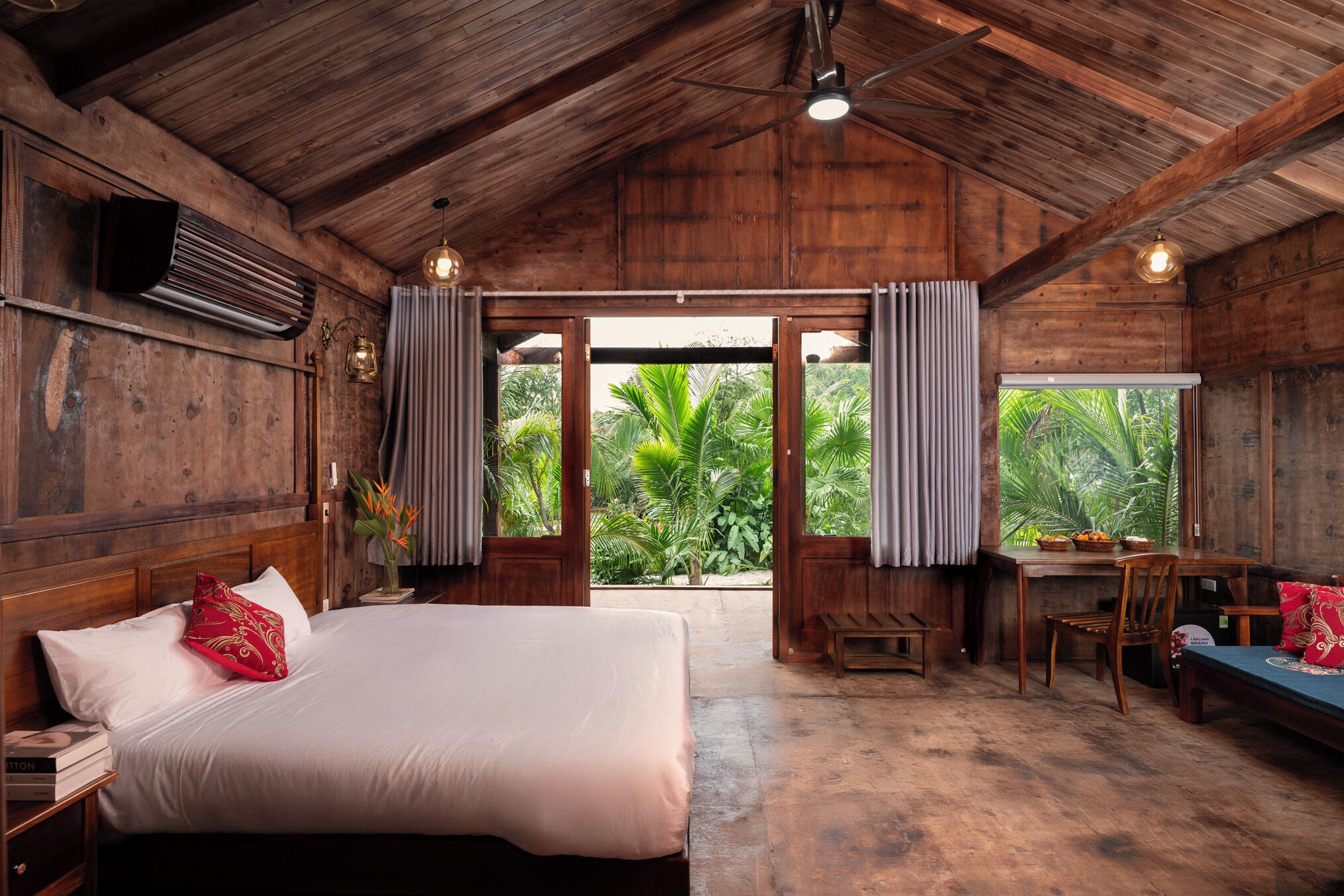 Ein Zimmer mit Holzboden, einem Bett, einem Schreibtisch und Blick auf üppiges Grün.