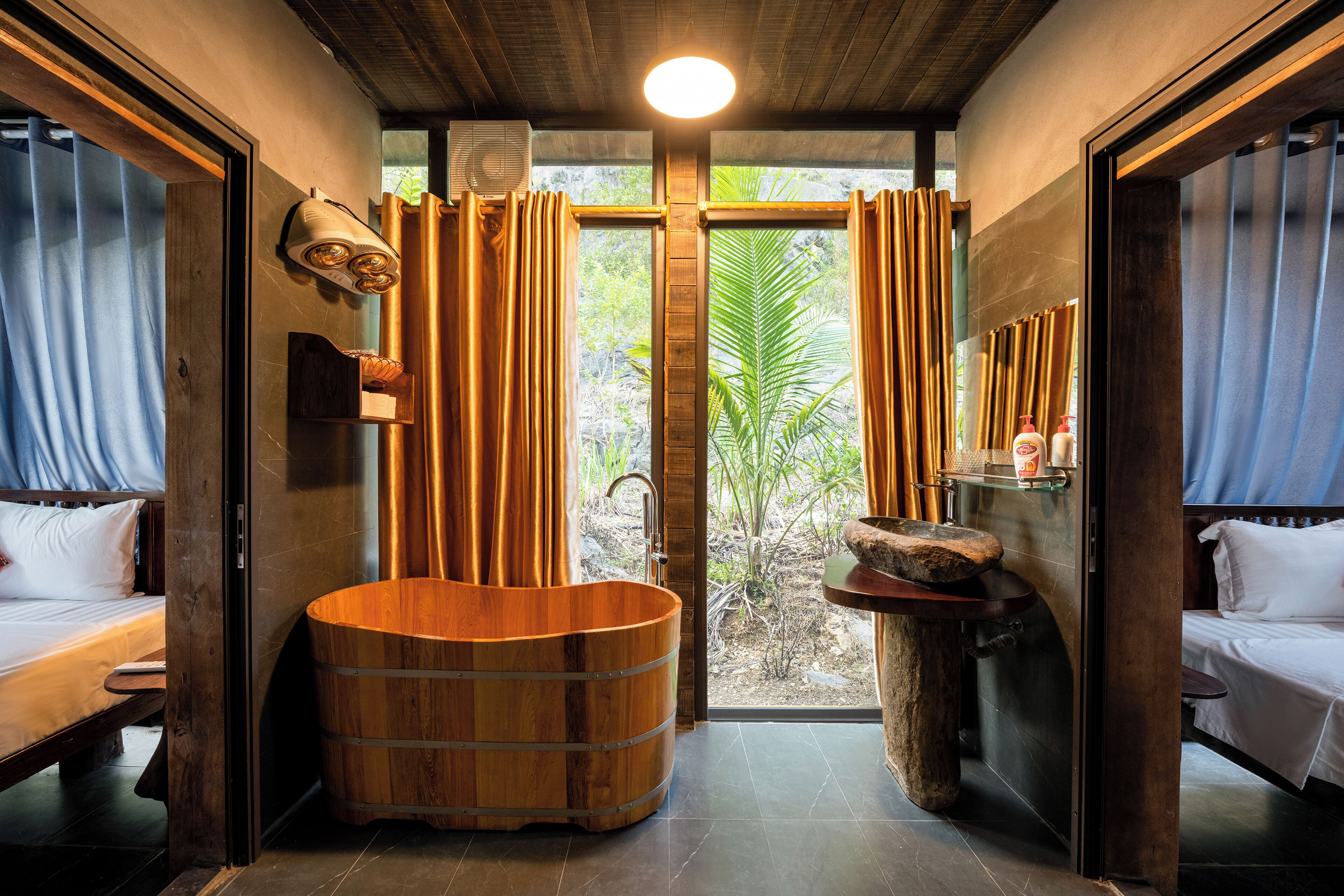 Una habitación con una bañera de madera, dos camas, un lavamanos pequeño y un ventanal con cortinas.