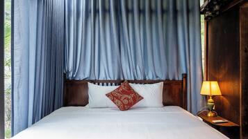 Una cama con sábanas blancas, un cojín estampado en rojo y un cabecero de madera.