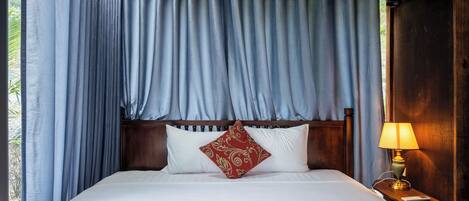 A bed with white linens, a red patterned pillow, and a wooden headboard.