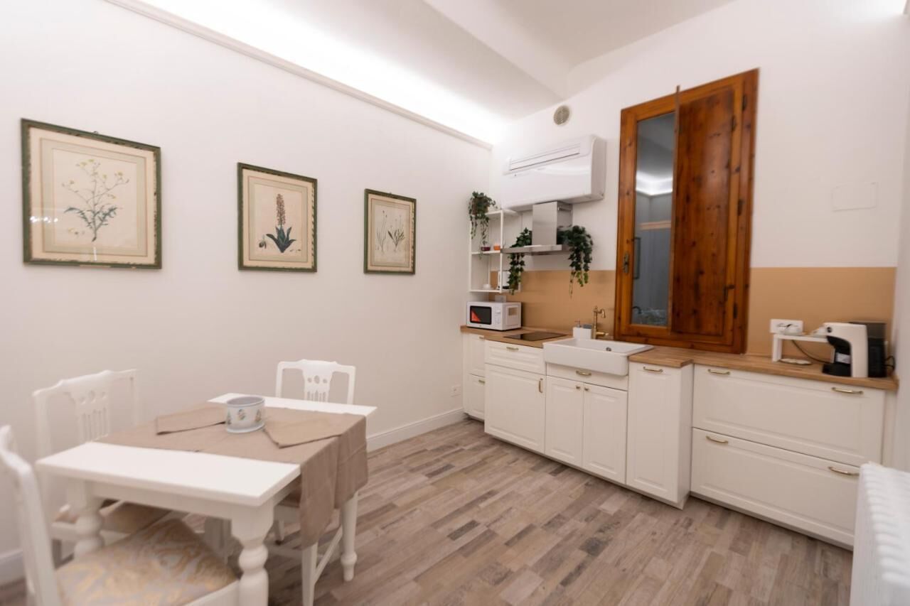 Une cuisine compacte avec des meubles blancs, un meuble en bois, un four à micro-ondes et un évier. Les murs sont ornés d’illustrations botaniques encadrées, et on y trouve une table avec des chaises.
