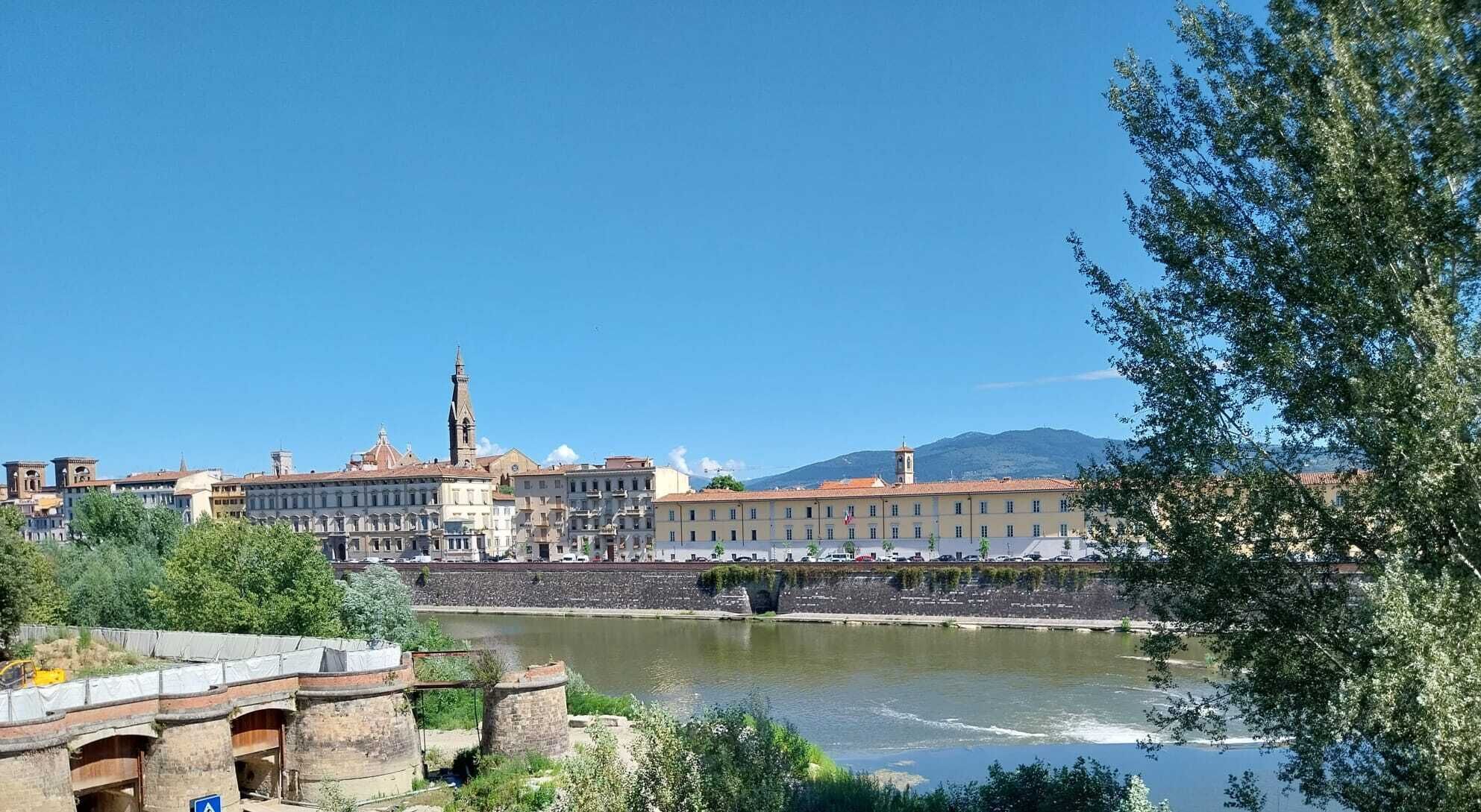 A riverside view of a historic town with buildings, a tower, and a bridge.