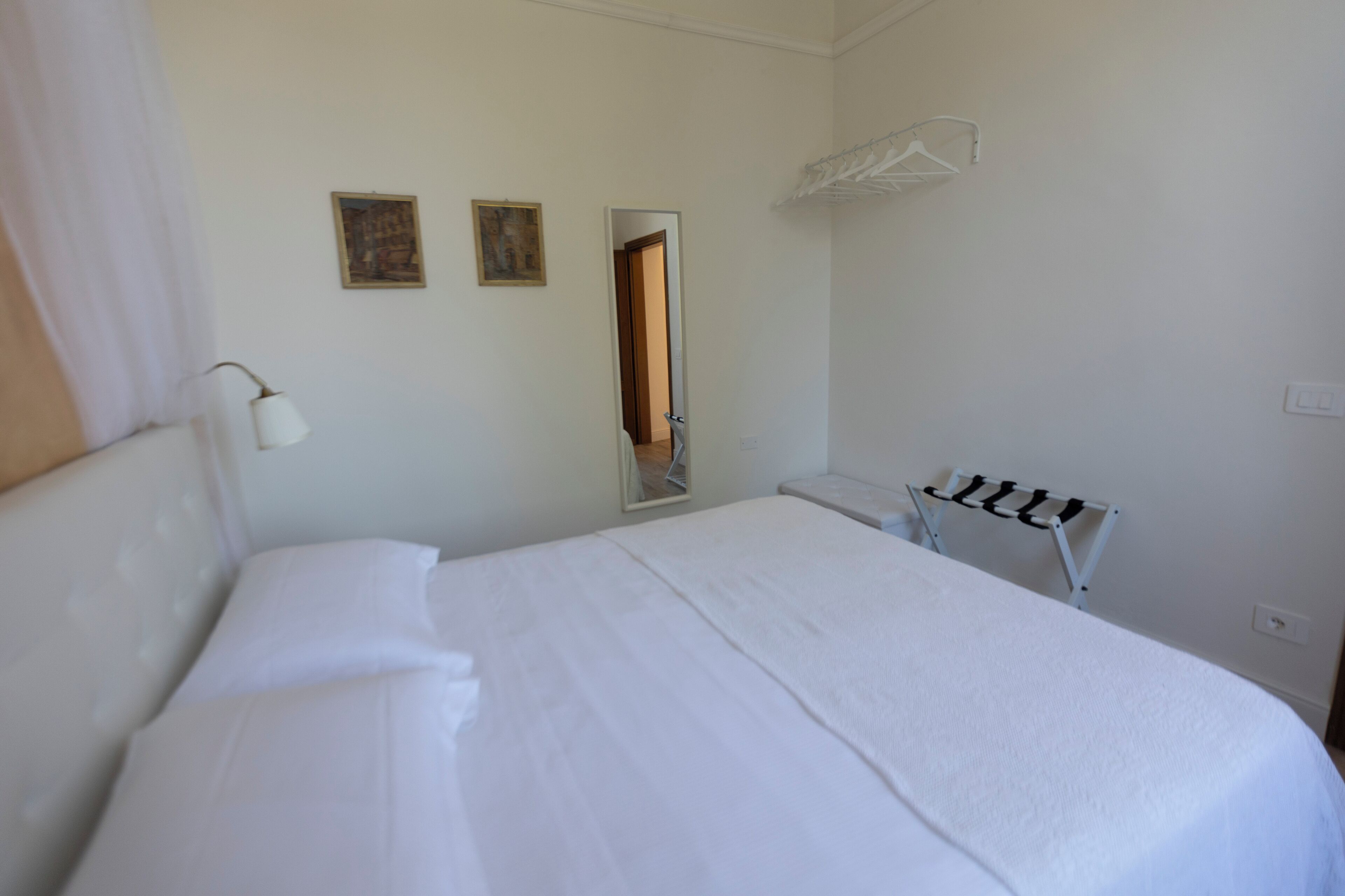 A hotel room with a large bed, a bedside table, a mirror, and a wall-mounted towel rack.