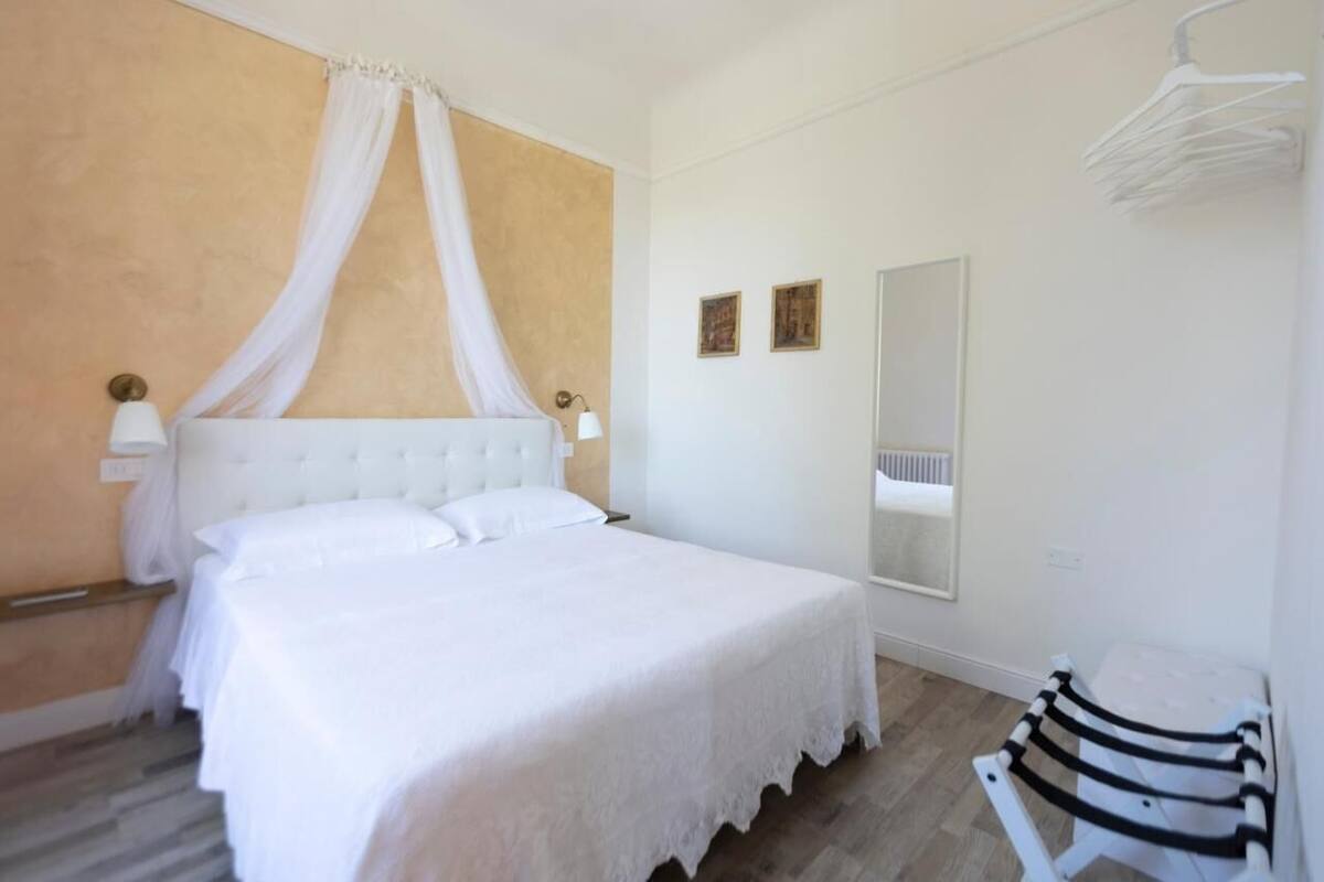 A bedroom with a large bed, a canopy, a bedside table, a mirror, and a chair.