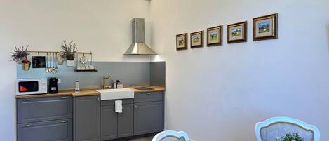 A modern kitchen with grey cabinets, a wooden countertop, and a stainless steel range hood. There are framed pictures on the wall and a dining table with chairs.