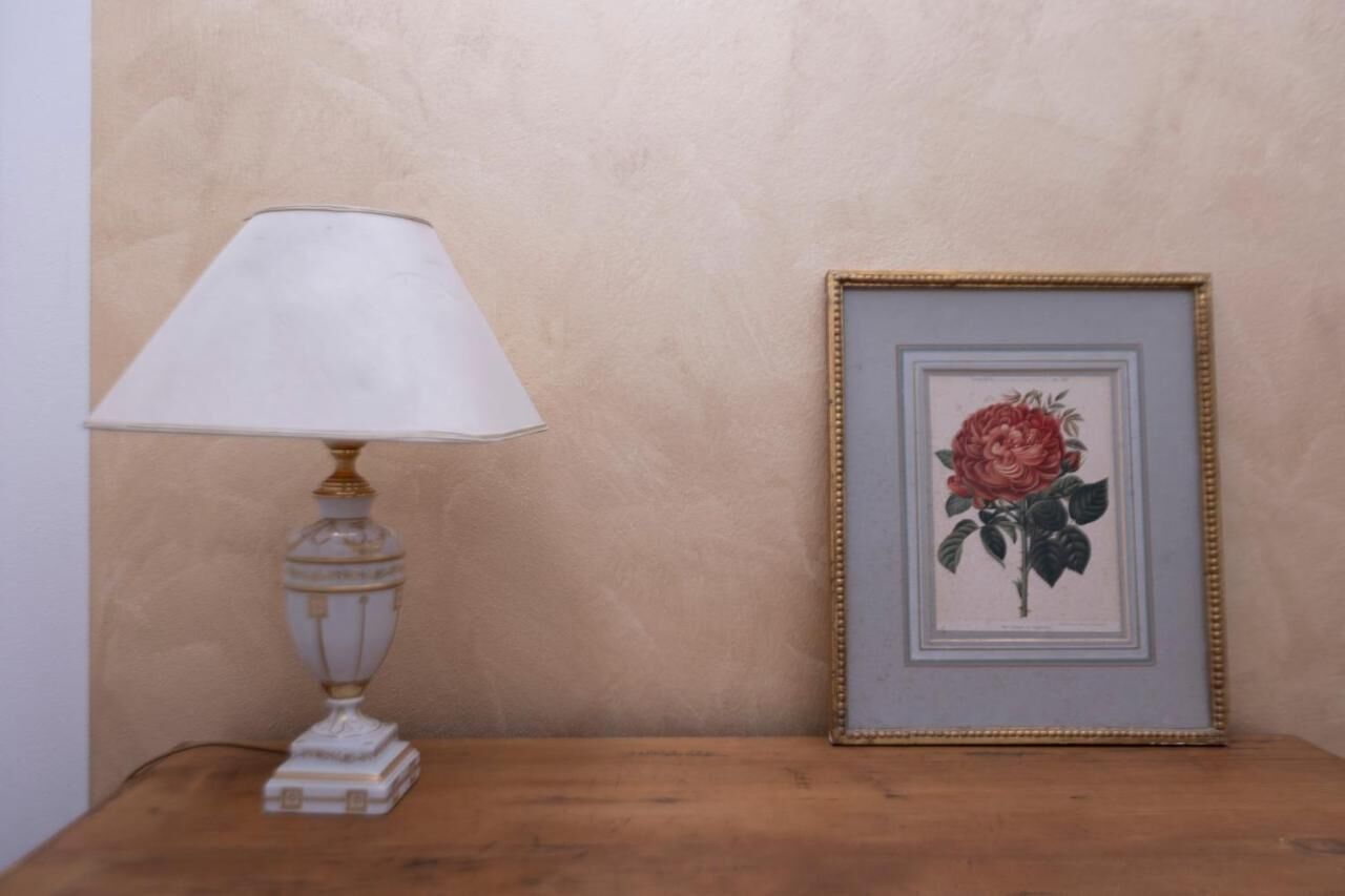 Una mesa con una lámpara blanca y un cuadro con una rosa.