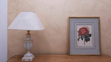 Una mesa con una lámpara blanca y un cuadro con una rosa.