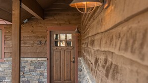 A wooden log cabin entrance with a stone wall, a wooden door marked "26 A", and a hanging light fixture. - Condo with Private Hot Tub and Balcony Views | 5 Minutes to Ski Base (Big Sky)