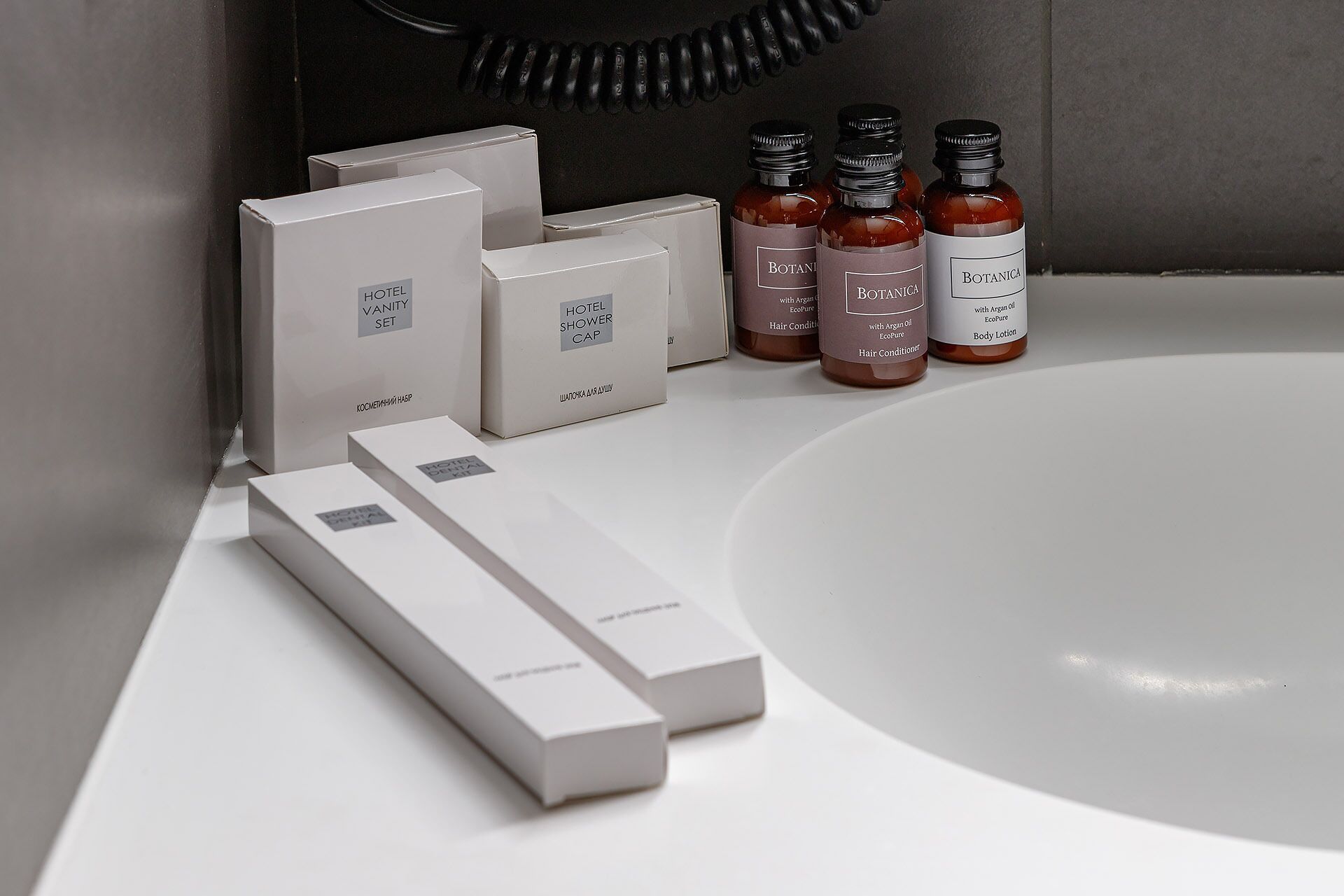 Une salle de bain avec un lavabo blanc, plusieurs articles de toilette, notamment un après-shampoing et une lotion pour le corps, ainsi qu’un bonnet de douche.