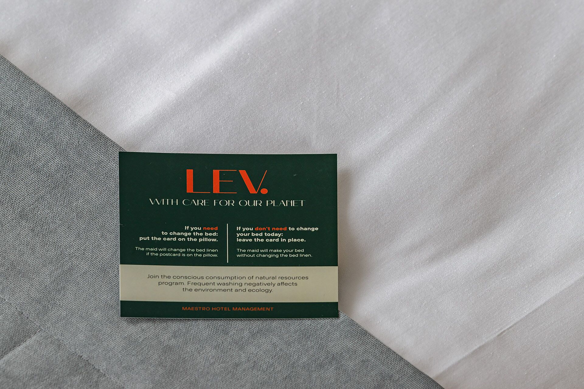 Une carte d’information sur la gestion de l’hôtel, posée sur le lit, avec des instructions sur l’entretien du linge de lit.