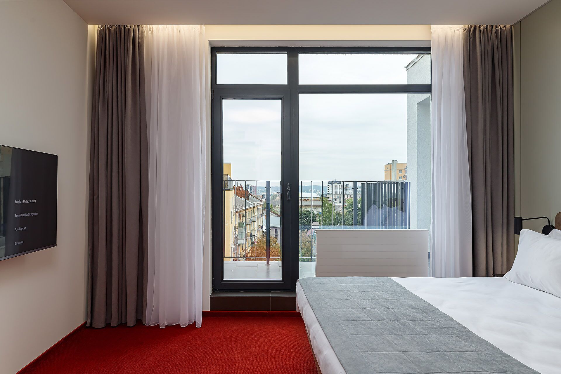 A hotel room with a large sliding glass door to a balcony, a bed with white bedding, and a flat-screen TV mounted on the wall.