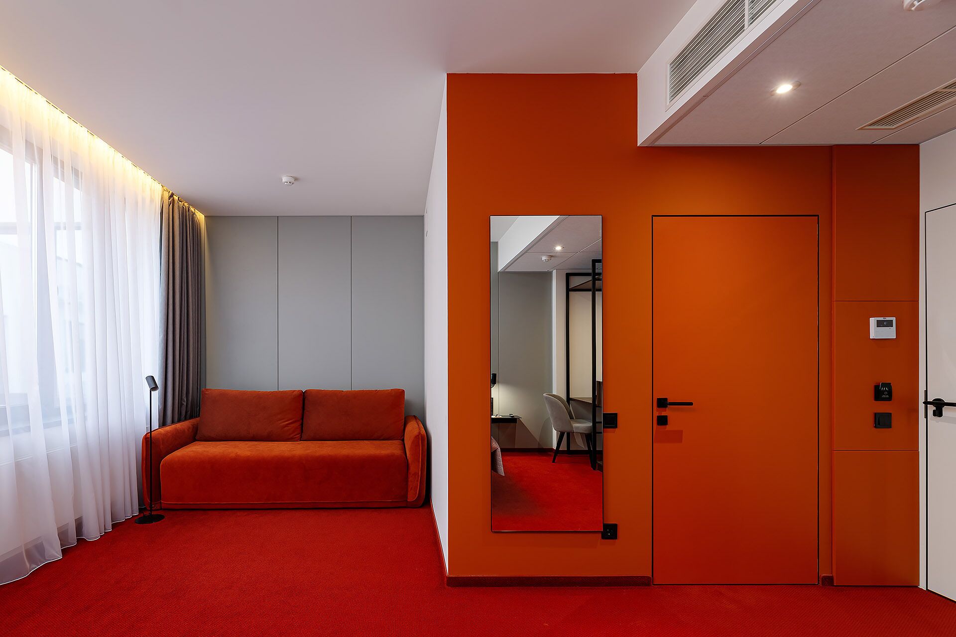 Habitación de hotel con alfombra roja, un sofá, un armario y un espejo.