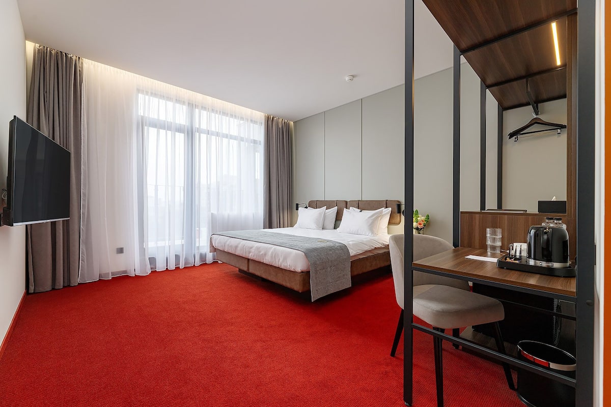 Hotellihuone, jossa on suuri sänky, työpöytä tuolilla, taulutelevisio ja peili.