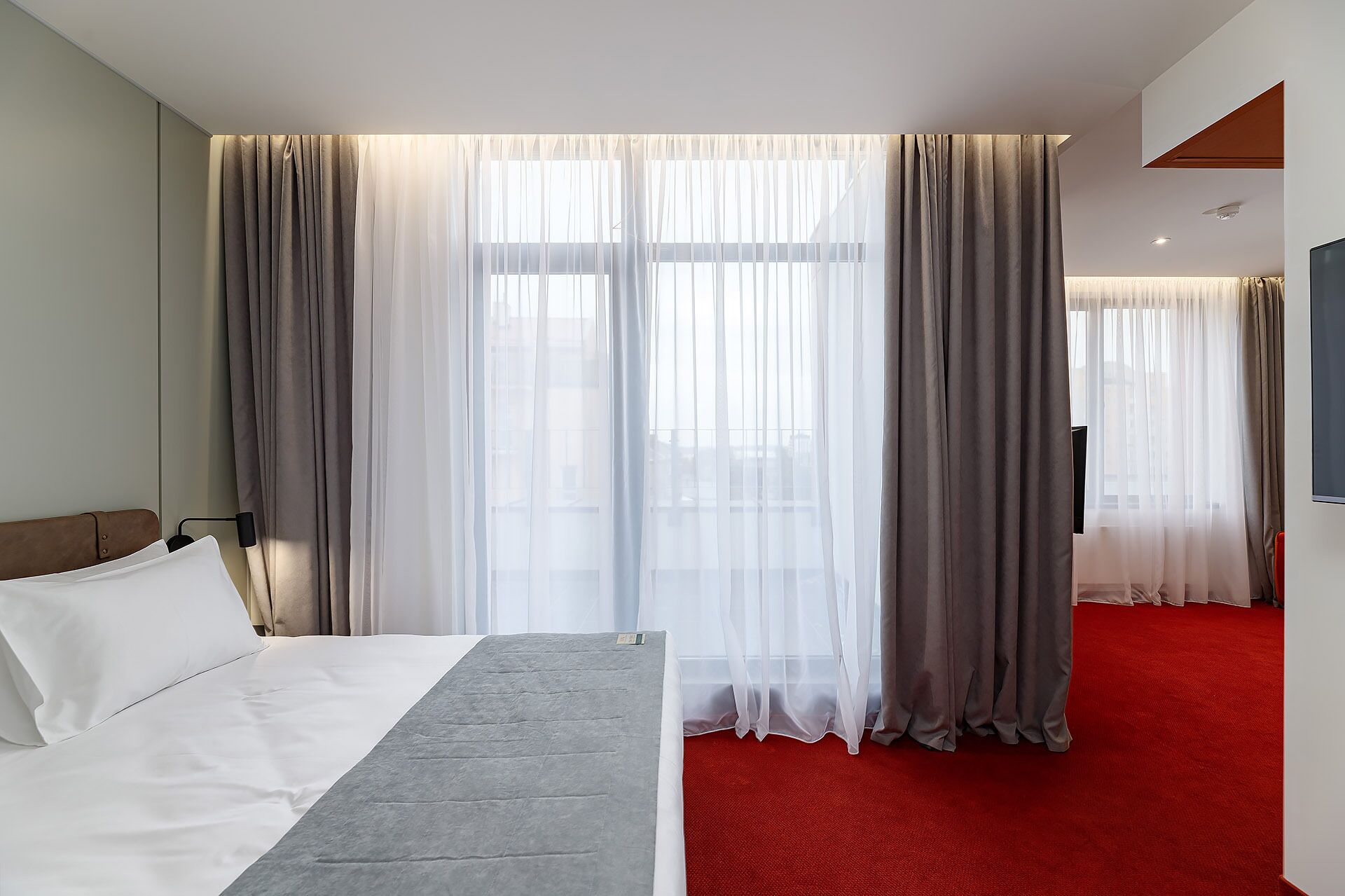 A hotel room with a bed, a TV, and a red carpet.