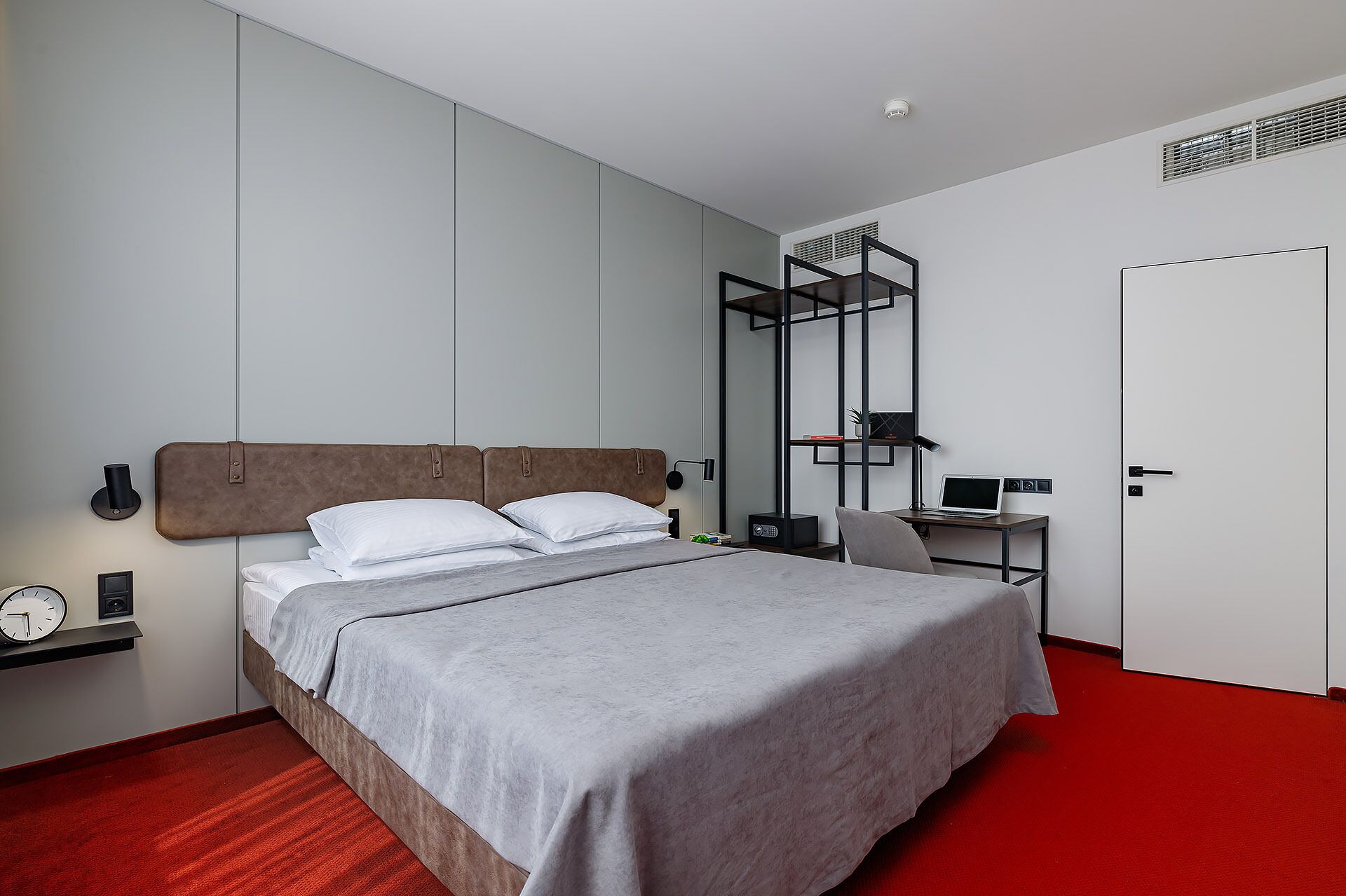 A modern hotel room with a bed, a desk, and a wardrobe.