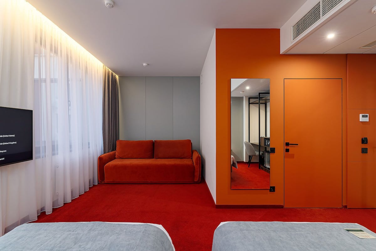 Hotellihuone, jossa on punainen matto, sohva, televisio ja peili.